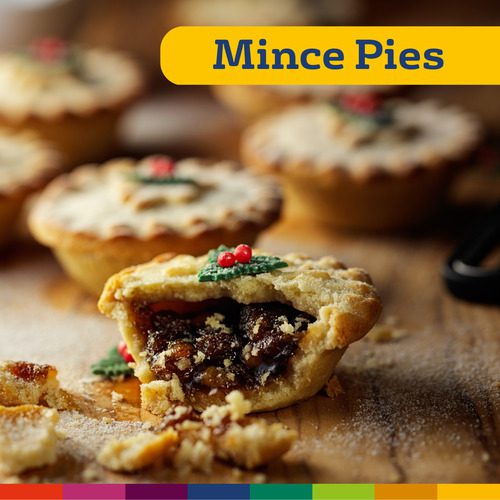 Um close de uma torta de carne moída quebrada mostrando seu recheio de frutas, com tortas de carne moída inteiras ao fundo e "Mince Pies" escrito no topo, evocando o espírito festivo do Natal em Manchester.