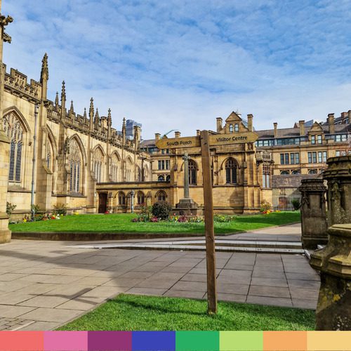 Uno storico edificio in pietra con finestre ad arco e un cortile con giardino, che ricorda la Cattedrale di Manchester. Un cartello in legno indica "South Porch" e "Visitor Centre". Cielo azzurro con nuvole sparse.