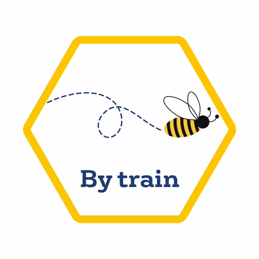 A hexagon with a yellow border contains a cartoon bee and the words "By train" in blue text, highlighting public transport in Manchester.