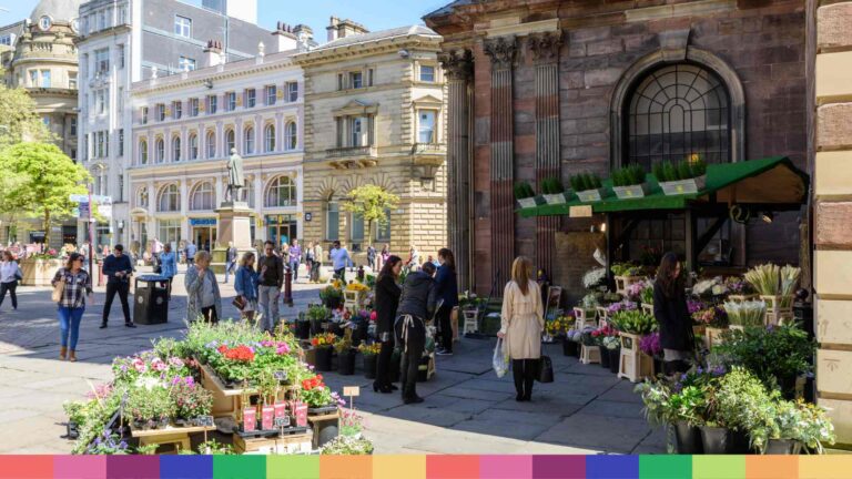 La gente mira y compra flores en un puesto de flores al aire libre en una concurrida plaza de la ciudad con edificios históricos: una de las muchas cosas gratis para hacer en Manchester.